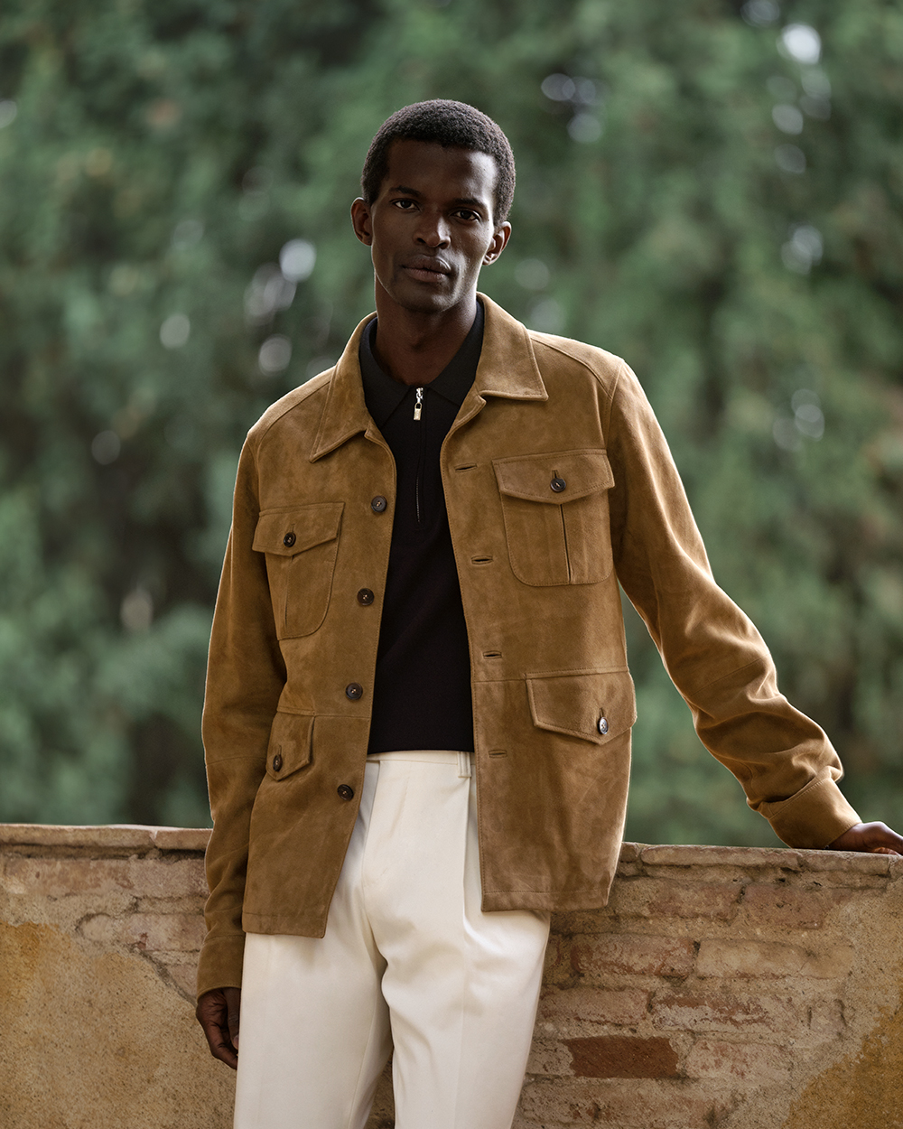 man in suede jacket with white trousers and a black half-zip